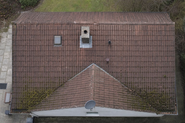 Cały dach domu z kominem, oknem dachowym i widocznym stanem pokrycia sfotografowany pionowo z drona - materiał poglądowy